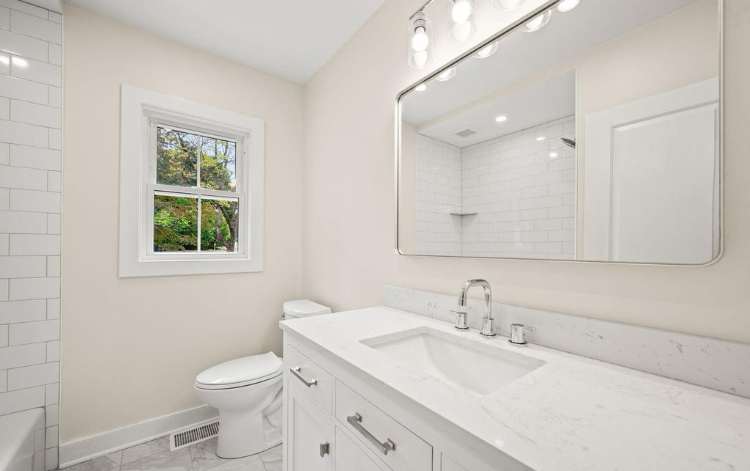 Full bathroom with white vanity, quartz counter, and tiled shower