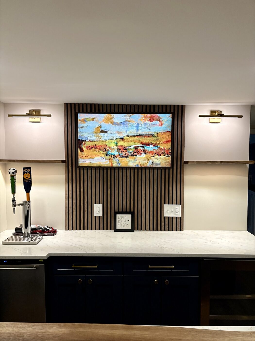 Wet bar with wood slat feature wall, shelves, and brass picture lights